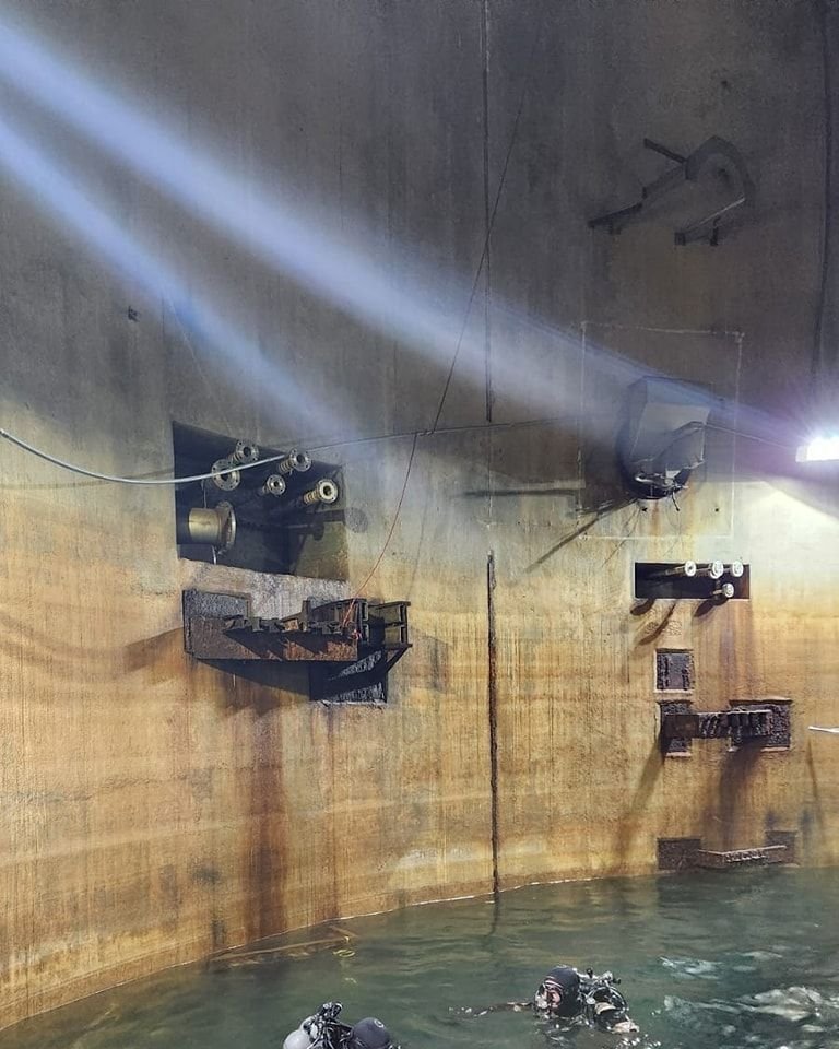 Inside the silo, the flooded interior feels vast and cathedral-like, with beams, platforms, and shadowy structure suspended in remarkably clear water.