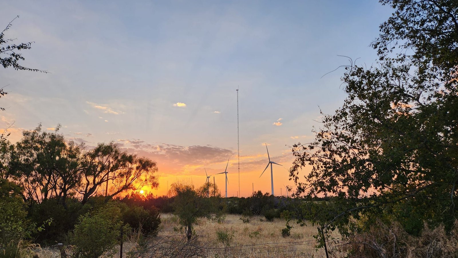 Outside the Valhalla site at sunset, the Texas landscape opens wide under soft evening light, with wind turbines on the horizon and a quiet, cinematic stillness that sets the tone before you ever step below ground.